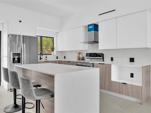 kitchen featuring a breakfast bar area, stainless steel appliances, light countertops, wall chimney range hood, and modern cabinets