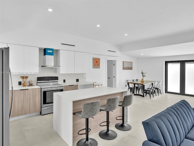 kitchen featuring wall chimney range hood, light countertops, appliances with stainless steel finishes, a kitchen breakfast bar, and modern cabinets