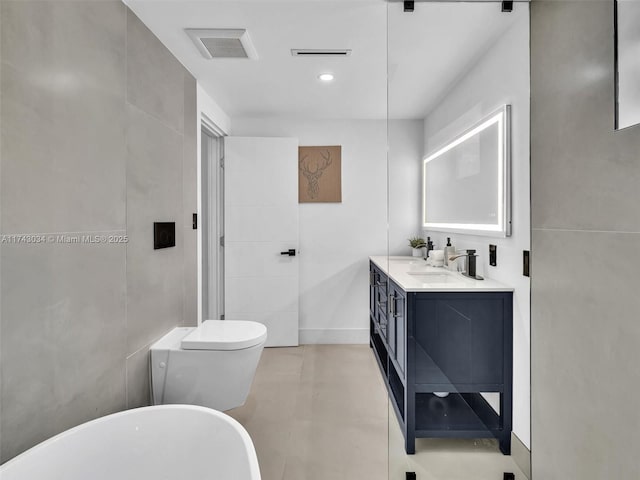 bathroom featuring tile walls, a freestanding tub, visible vents, and a sink