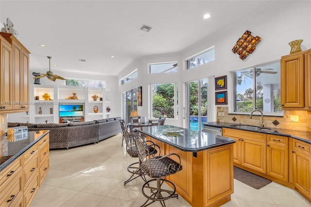 kitchen with a sink, a kitchen breakfast bar, open floor plan, a center island, and dark stone counters