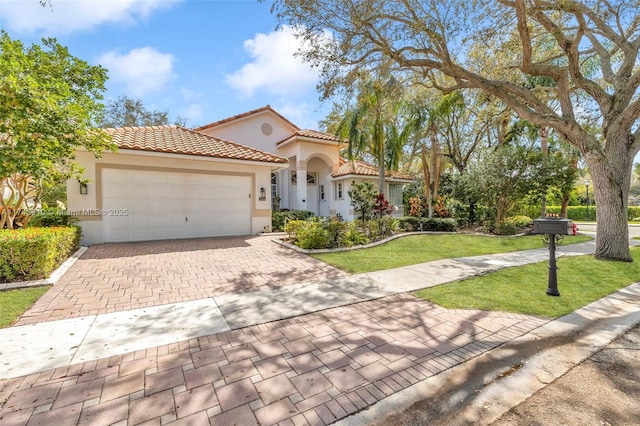 mediterranean / spanish house featuring decorative driveway, a tile roof, stucco siding, a garage, and a front lawn