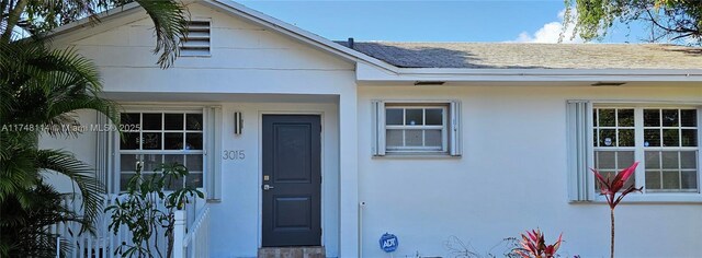 property entrance featuring stucco siding and roof with shingles