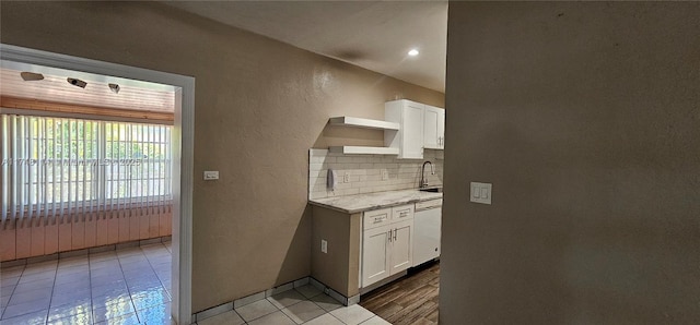 kitchen featuring white cabinets, backsplash, dishwasher, a textured wall, and a sink