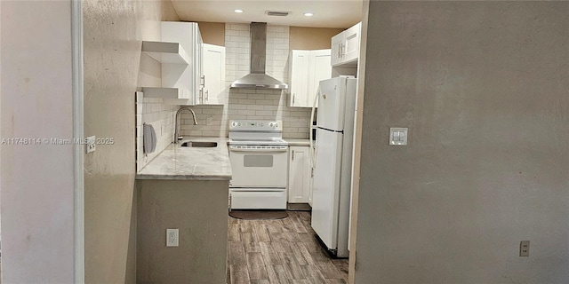 kitchen featuring a sink, decorative backsplash, wall chimney exhaust hood, white appliances, and wood finished floors