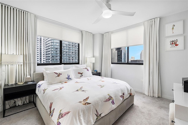 bedroom with baseboards, a view of city, a ceiling fan, and light colored carpet