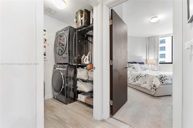 laundry room featuring light wood-type flooring, stacked washing maching and dryer, visible vents, and laundry area