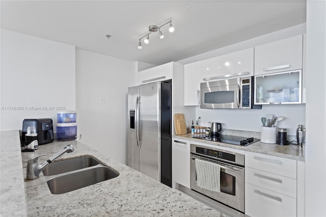 kitchen with stainless steel appliances, white cabinetry, a sink, and light stone countertops