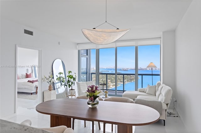 dining area featuring light tile patterned floors, a water view, visible vents, expansive windows, and baseboards