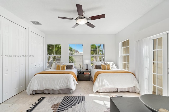 bedroom with visible vents, ceiling fan, and two closets