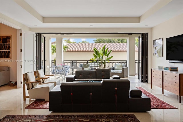 living area with ceiling fan, a raised ceiling, and a healthy amount of sunlight