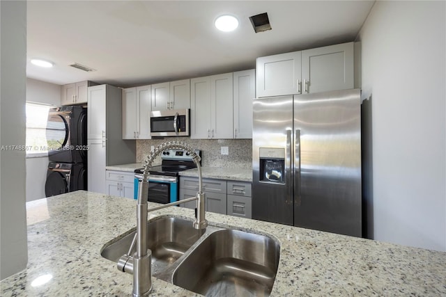 kitchen featuring a sink, stacked washing maching and dryer, appliances with stainless steel finishes, and light stone counters