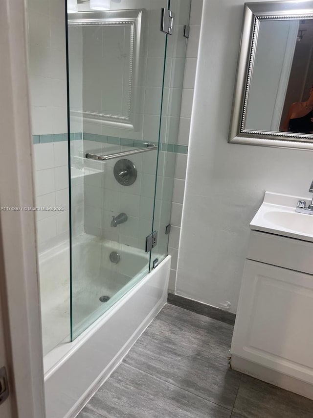 full bath with bath / shower combo with glass door, wood finished floors, and vanity