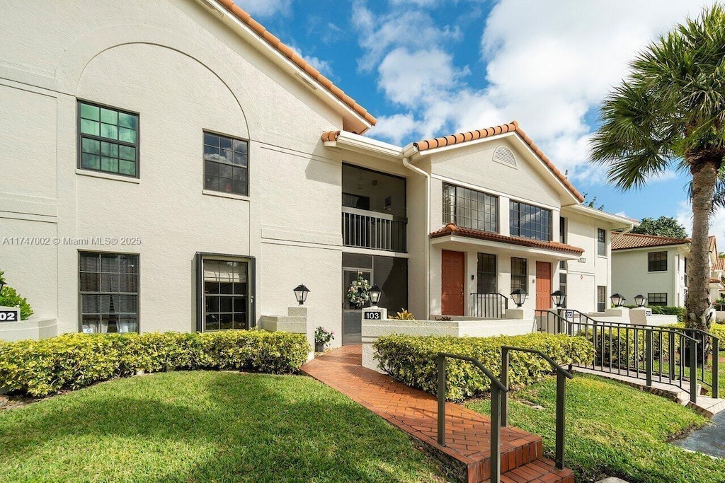 view of front facade featuring a tiled roof, a front lawn, and stucco siding