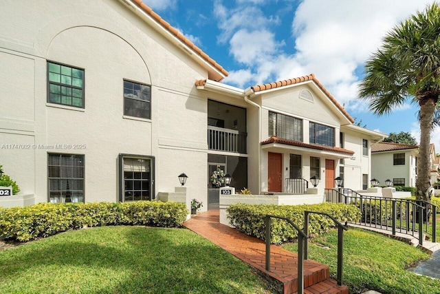 view of front facade featuring a tiled roof, a front lawn, and stucco siding