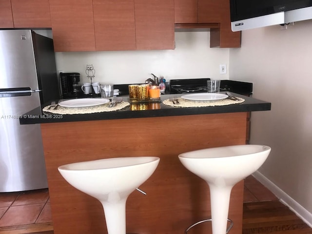 kitchen featuring dark countertops, tile patterned flooring, baseboards, and freestanding refrigerator