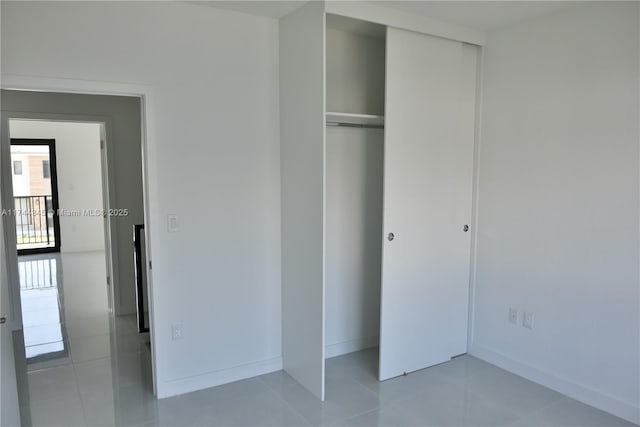 unfurnished bedroom with a closet, light tile patterned flooring, and baseboards