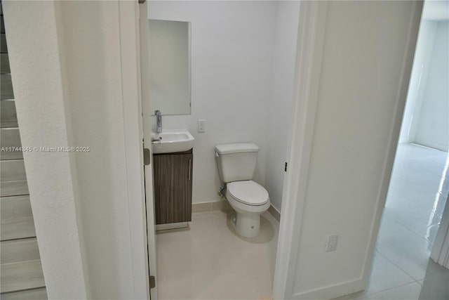 half bathroom with toilet, tile patterned flooring, baseboards, and vanity