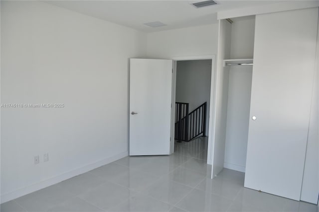 unfurnished bedroom featuring a closet, light tile patterned flooring, visible vents, and baseboards