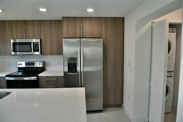 kitchen with appliances with stainless steel finishes, stacked washer / dryer, brown cabinetry, and recessed lighting