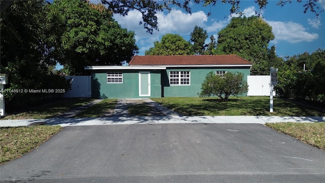 view of front of house featuring aphalt driveway, a tile roof, stucco siding, fence, and a front lawn