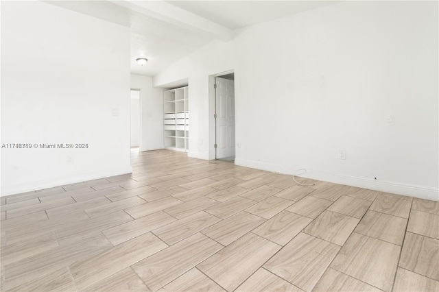 spare room with wood tiled floor, lofted ceiling with beams, and baseboards