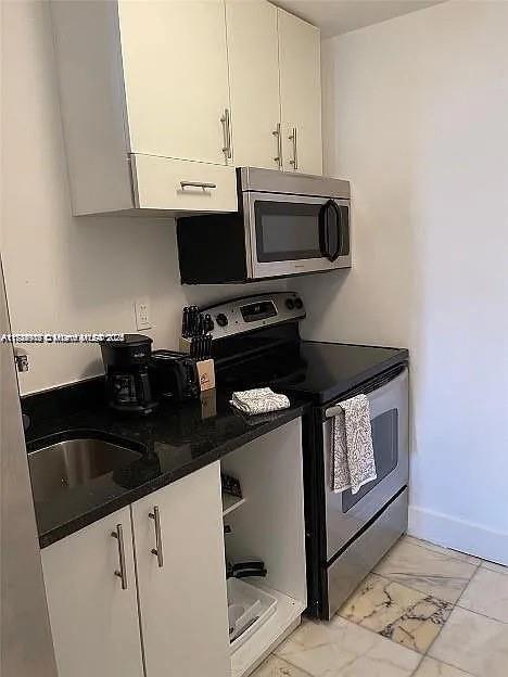 kitchen featuring stainless steel appliances, white cabinetry, baseboards, marble finish floor, and dark countertops