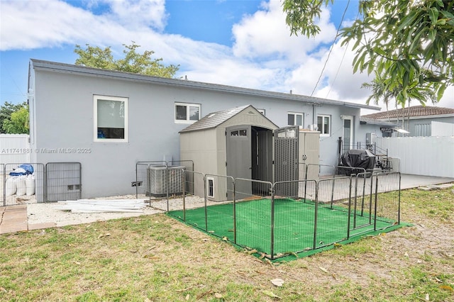 rear view of house with central AC unit, a yard, fence, and stucco siding