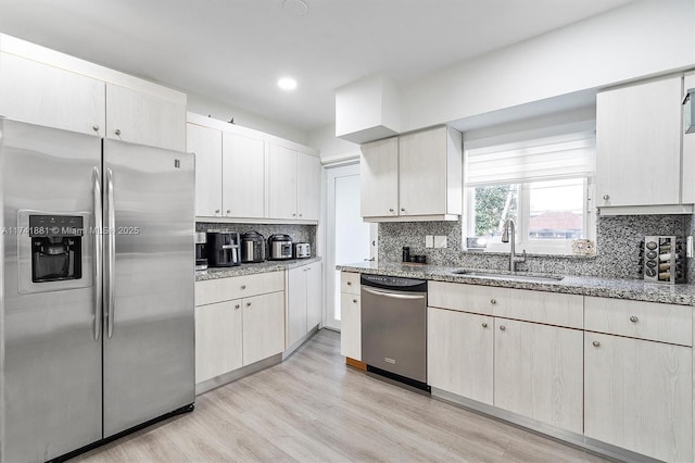 kitchen featuring appliances with stainless steel finishes, a sink, decorative backsplash, and light wood finished floors