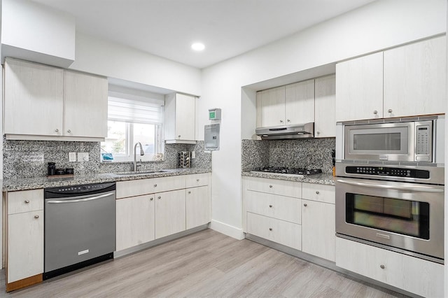 kitchen with decorative backsplash, appliances with stainless steel finishes, light stone countertops, under cabinet range hood, and a sink