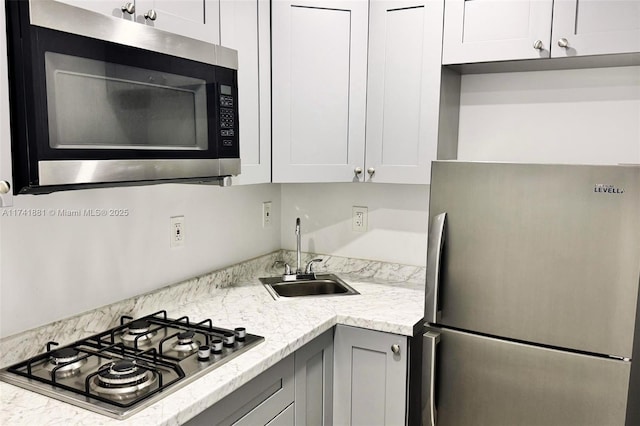 kitchen featuring appliances with stainless steel finishes, a sink, white cabinets, and light stone countertops