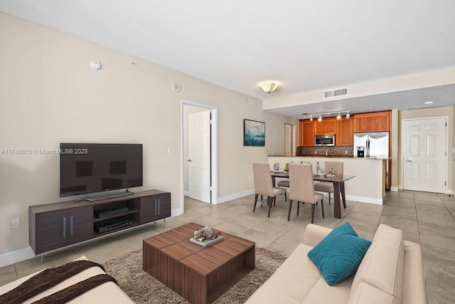 living room featuring light tile patterned floors, visible vents, a textured ceiling, track lighting, and baseboards