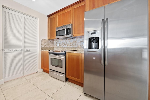 kitchen featuring light stone counters, light tile patterned floors, backsplash, appliances with stainless steel finishes, and brown cabinetry