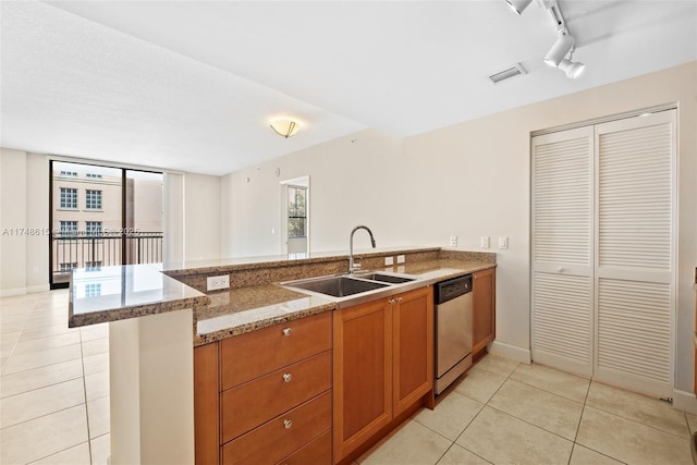 kitchen featuring light tile patterned floors, light stone counters, a sink, stainless steel dishwasher, and brown cabinetry