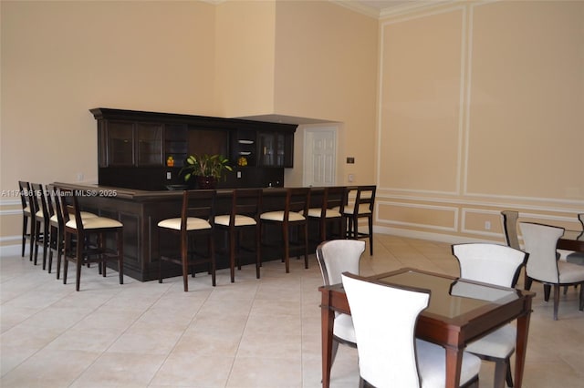 dining space with a community bar, light tile patterned floors, a high ceiling, and a decorative wall