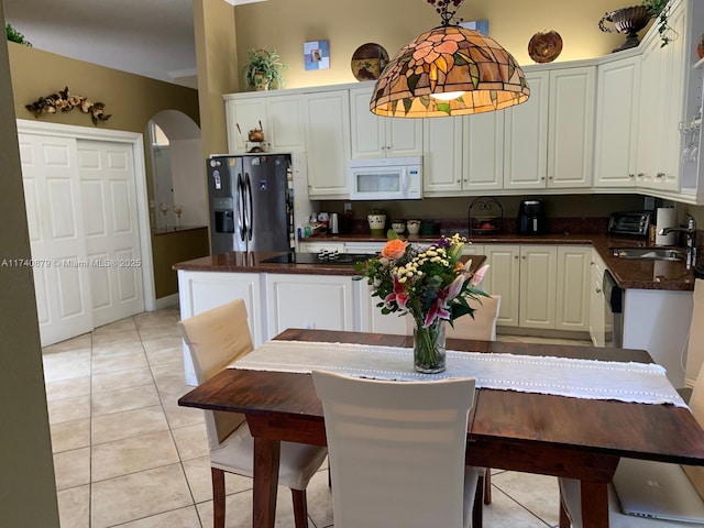 kitchen with arched walkways, stainless steel fridge with ice dispenser, dark countertops, white microwave, and a sink