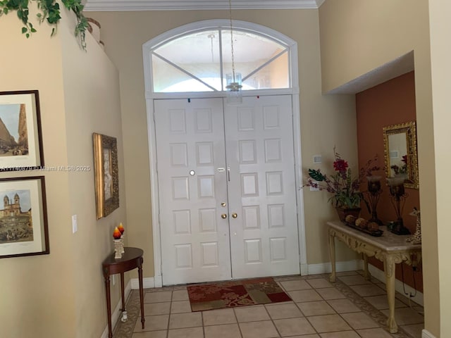 entryway with crown molding, a notable chandelier, baseboards, and light tile patterned floors