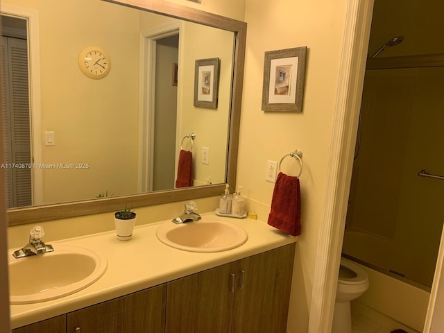 bathroom with shower / bath combination with glass door, a sink, toilet, and double vanity