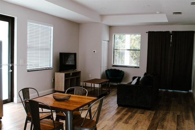 dining area featuring a raised ceiling, visible vents, baseboards, and wood finished floors