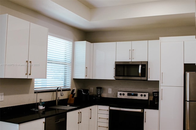 kitchen featuring stainless steel appliances, dark countertops, a sink, and white cabinetry