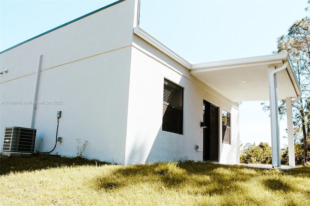 view of side of home with central air condition unit, a lawn, and stucco siding