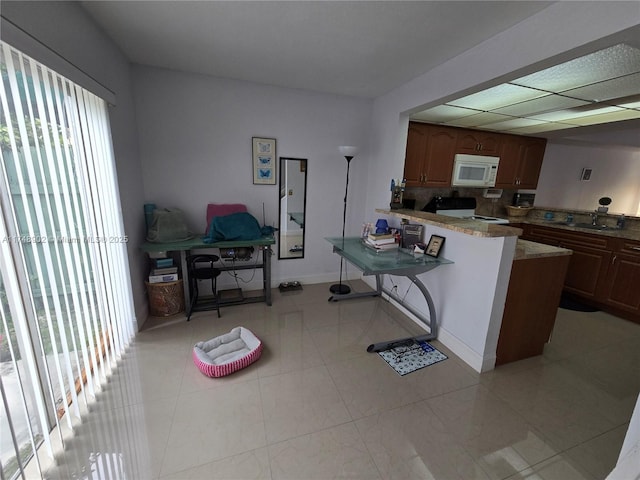 kitchen featuring white appliances, a peninsula, baseboards, and a sink