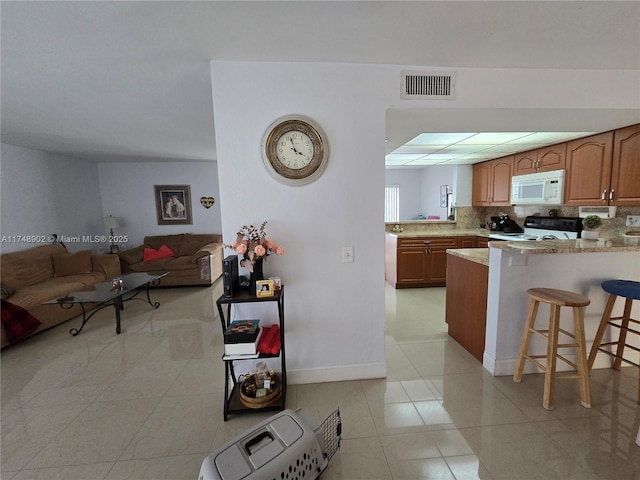 kitchen with white microwave, electric range oven, open floor plan, a kitchen bar, and visible vents