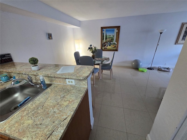 kitchen with tile patterned flooring, a peninsula, baseboards, light countertops, and a sink
