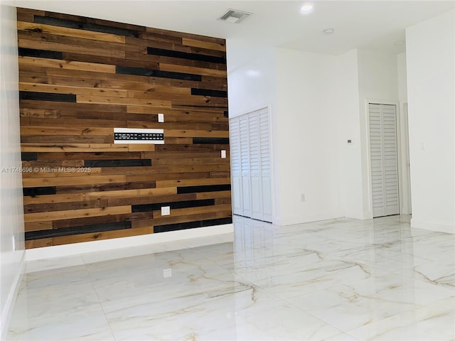 interior space with marble finish floor, visible vents, a high ceiling, wood walls, and baseboards