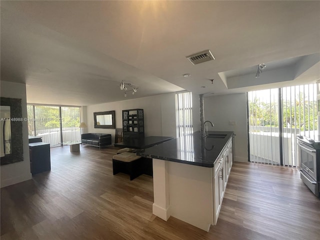 kitchen with a sink, visible vents, white cabinetry, open floor plan, and dark countertops