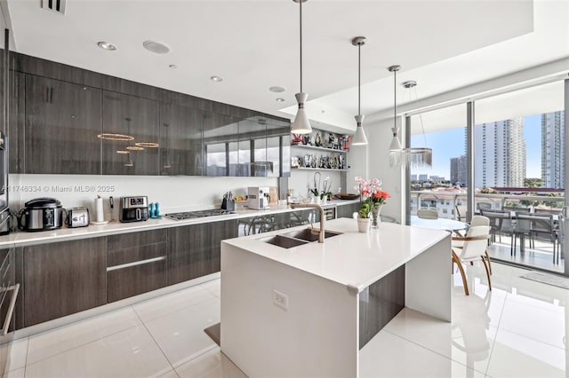 kitchen with a kitchen island with sink, light countertops, hanging light fixtures, a view of city, and modern cabinets