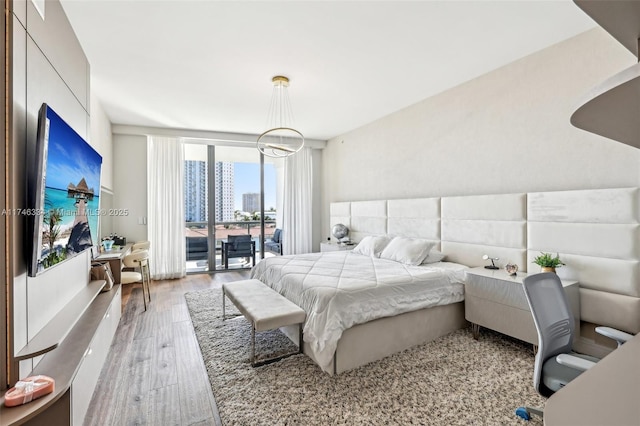 bedroom featuring access to exterior, a wall of windows, a city view, light wood-style floors, and a chandelier