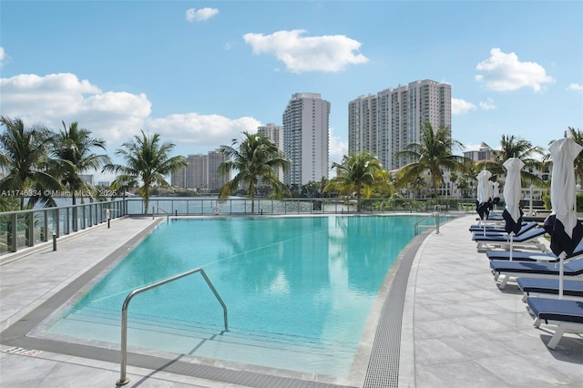 community pool with a view of city, a patio area, and fence