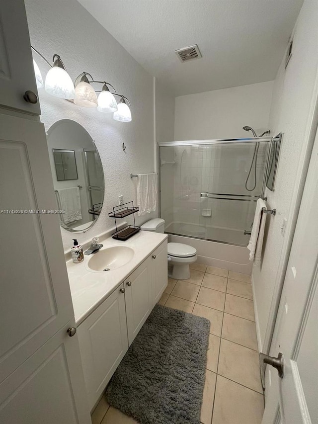 bathroom featuring shower / bath combination with glass door, visible vents, a textured wall, vanity, and tile patterned flooring