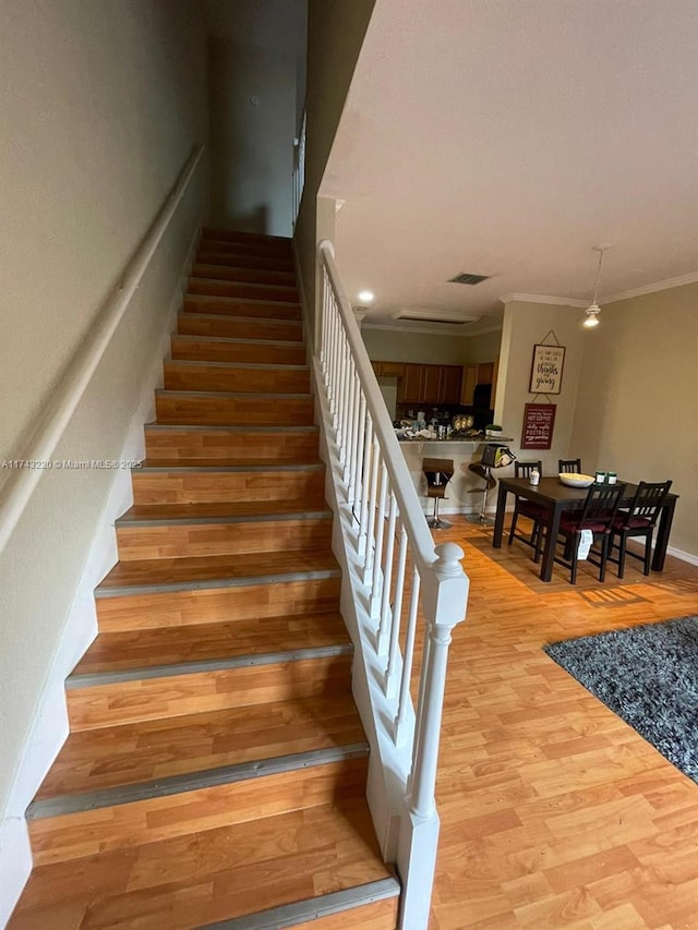 staircase with visible vents, crown molding, baseboards, and wood finished floors